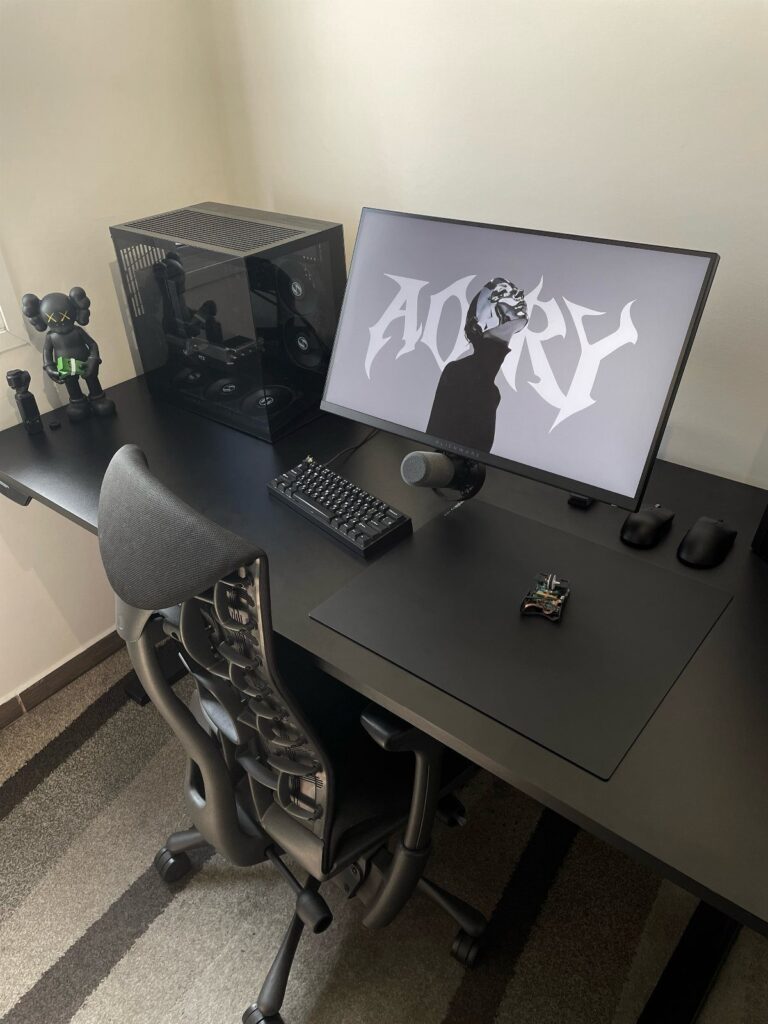 Black gaming setup with monitor, PC case, keyboard, and ergonomic chair on a desk.