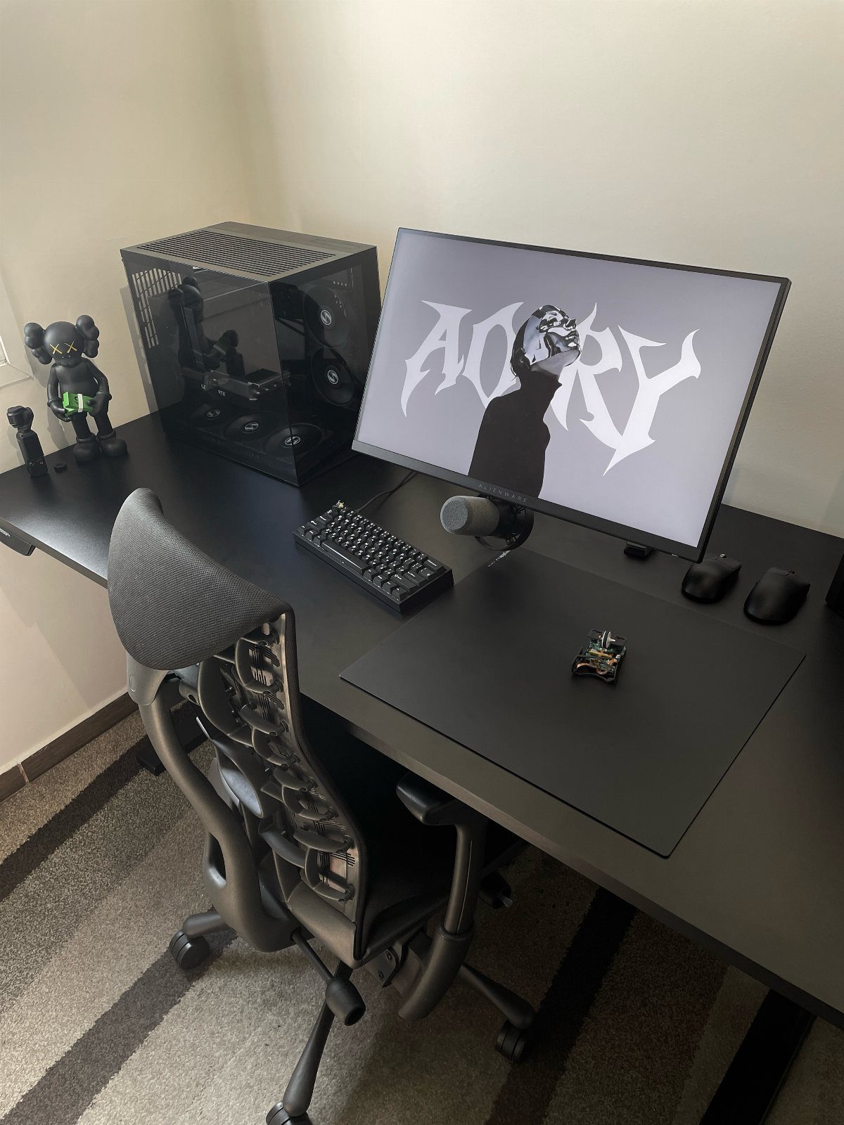 Black gaming setup with monitor, PC case, keyboard, and ergonomic chair on a desk.