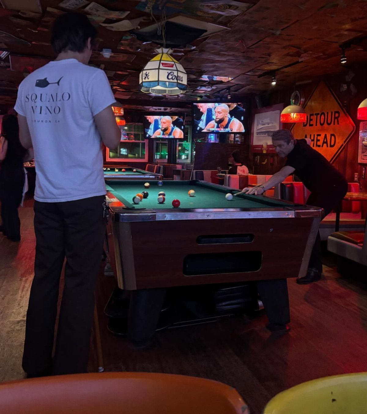 Man playing pool on a green table inside a rustic, dimly lit bar.