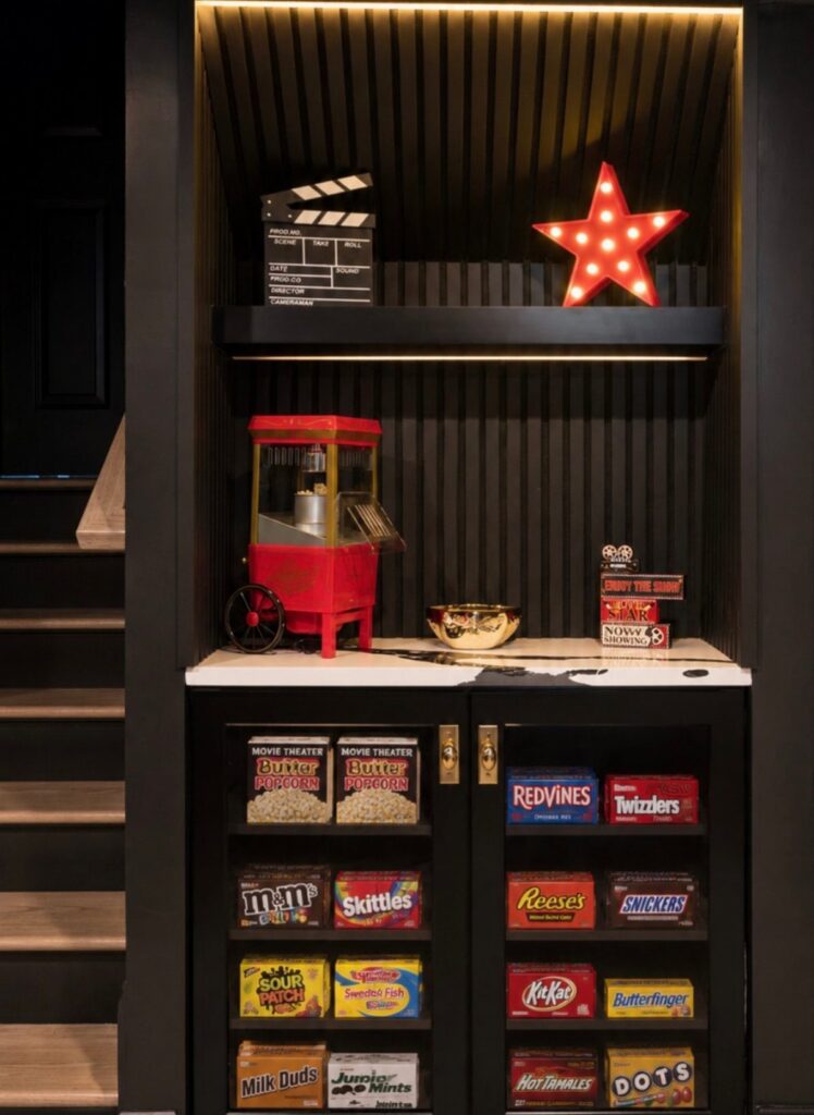 Movie themed snack station with popcorn machine and candy in a black cabinet.