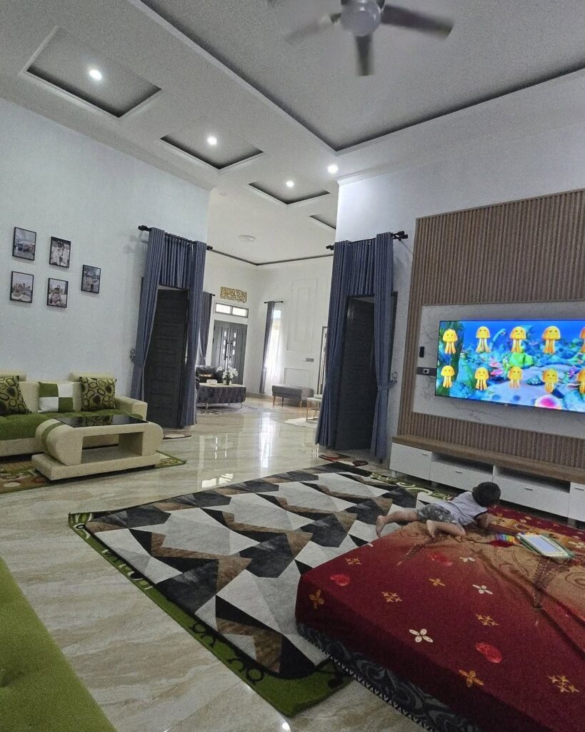 Living room with a large wall-mounted TV, geometric rug, and green sofa.