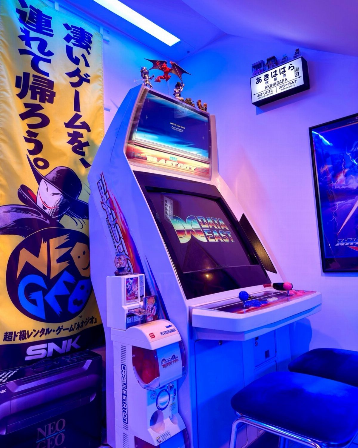 White arcade machine in a room with blue neon lighting and Japanese banners.