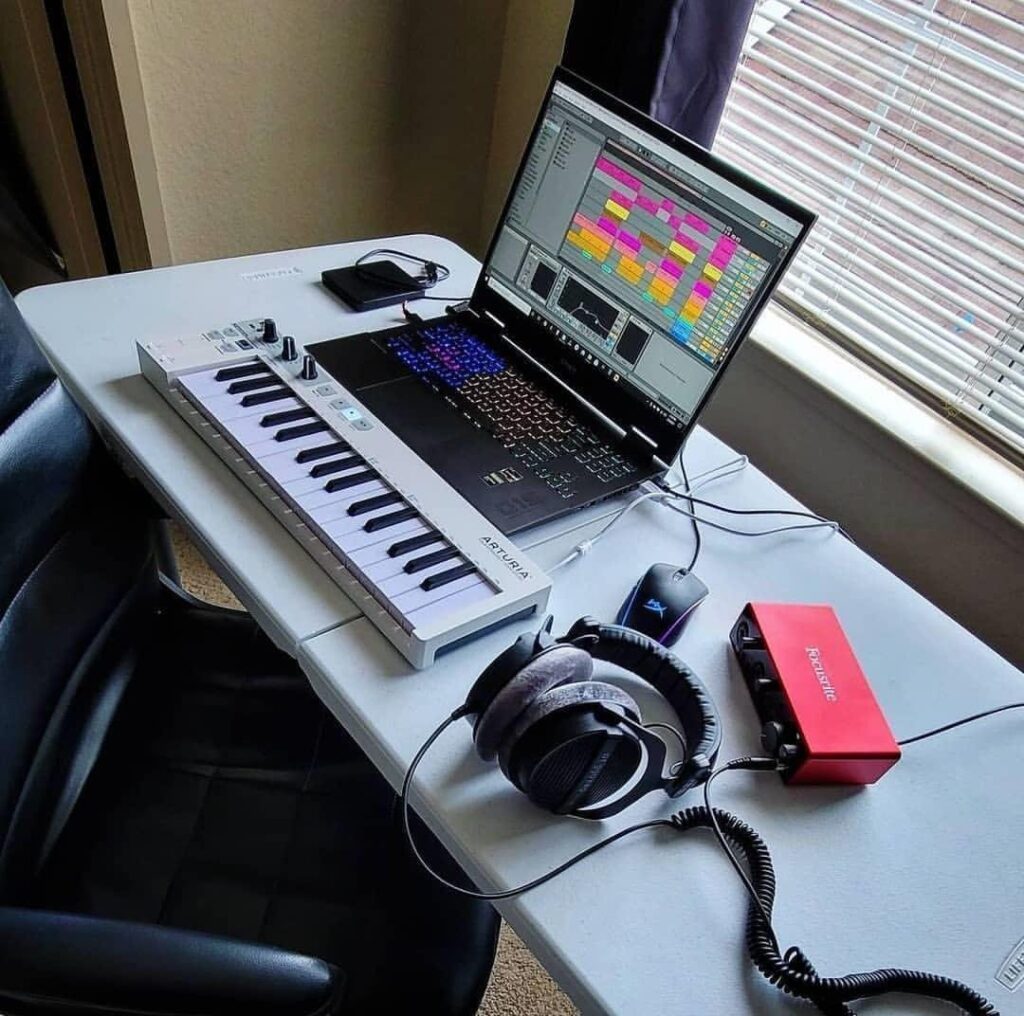 Home music studio setup with laptop, MIDI keyboard, audio interface, and headphones on desk