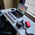 Home music studio setup with laptop, MIDI keyboard, audio interface, and headphones on desk