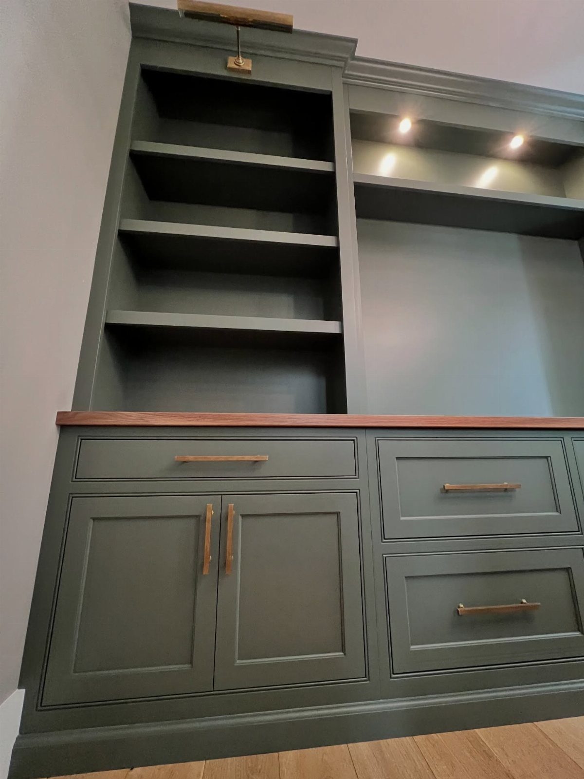 Sage green built-in home office cabinetry with open shelving and a wooden countertop.