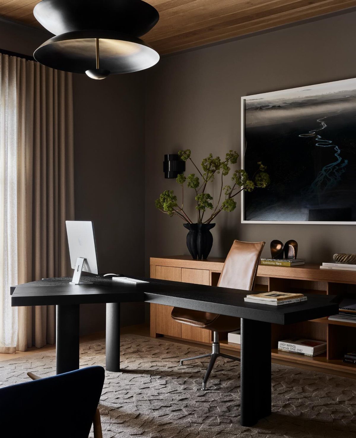 Modern home office with black L-shaped desk, leather chair, and abstract wall art.