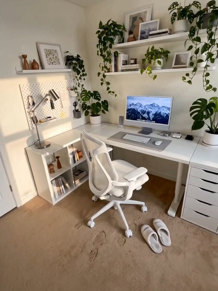 White small home office setup with a desk, ergonomic chair, and many green plants.