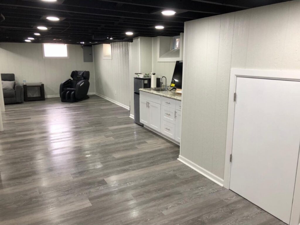 Finished basement with low black open-joist ceiling, grey flooring, and white walls.
