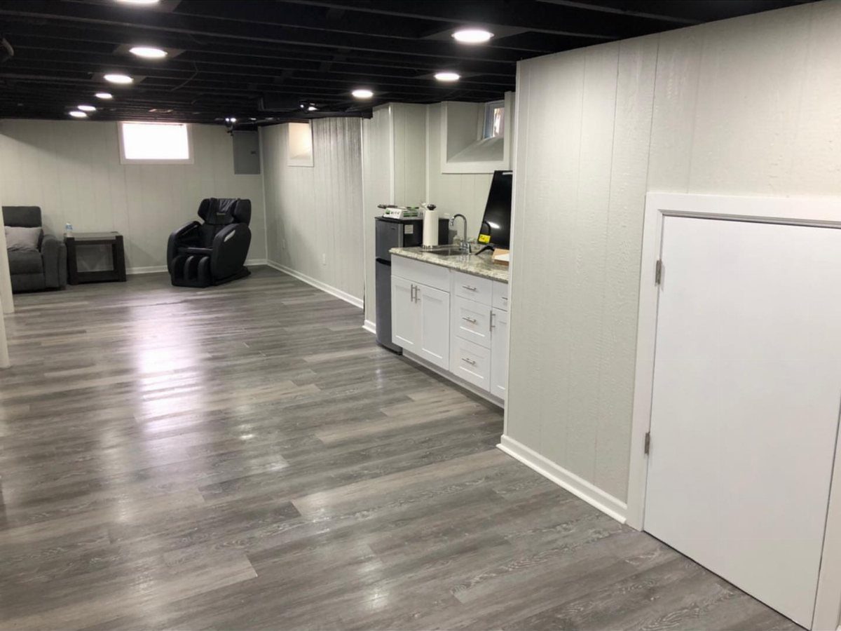 Finished basement with low black open-joist ceiling, grey flooring, and white walls.