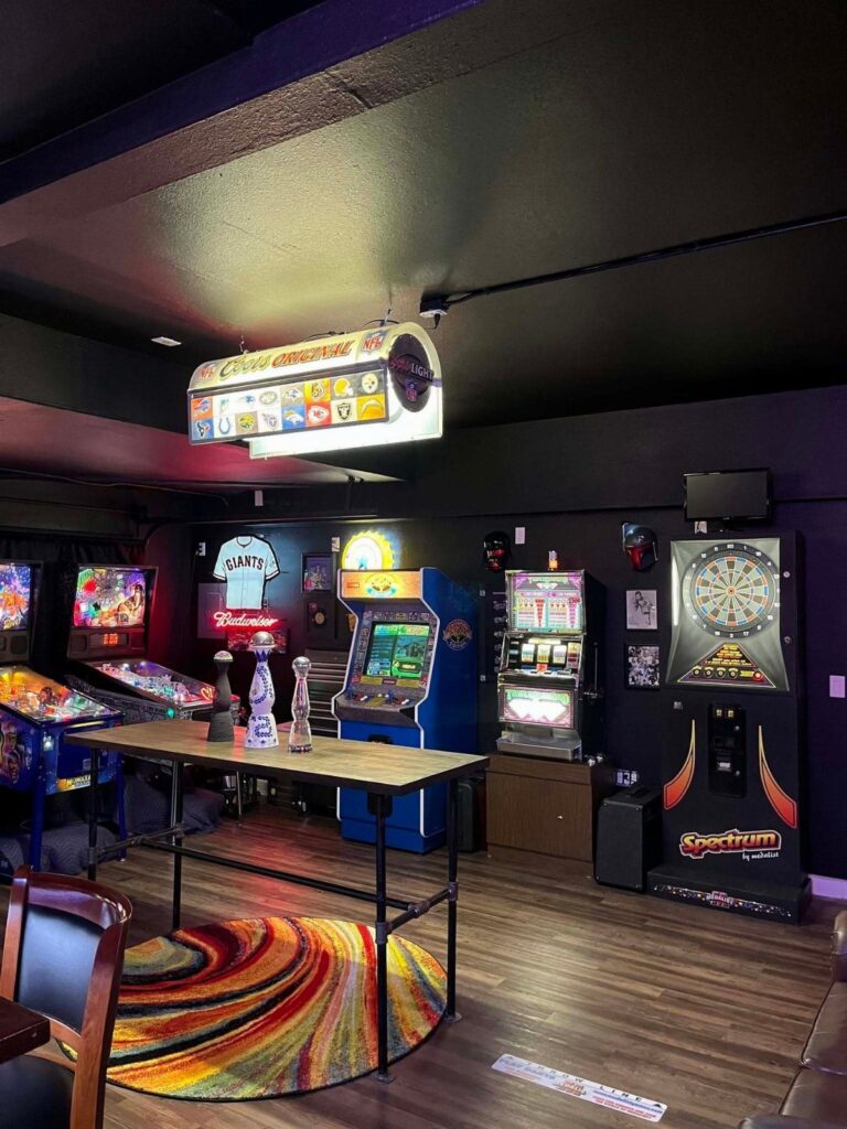 Blue arcade game machine and pinball machine in a dark themed man cave.