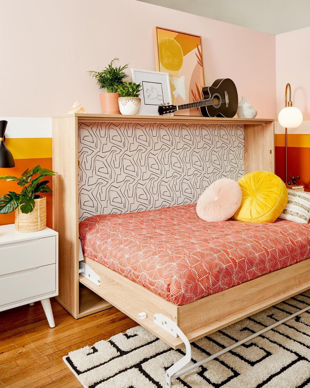 Horizontal Murphy bed with red bedding and yellow pillows in a colorful room.
