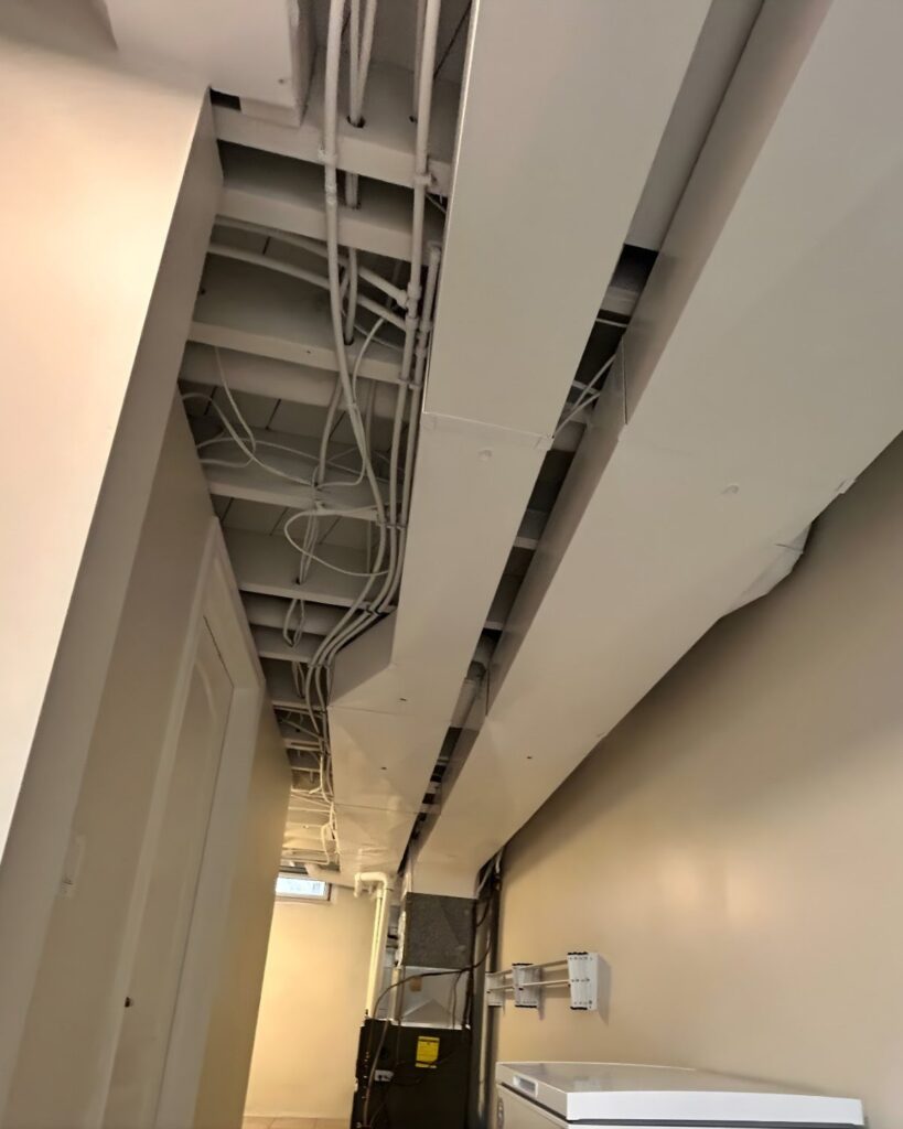 Unfinished basement ceiling with exposed joists and pipes painted in light grey.
