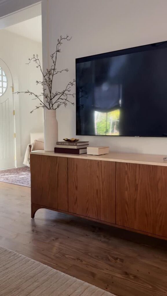 Wooden media console with a white vase and books under a wall-mounted television.