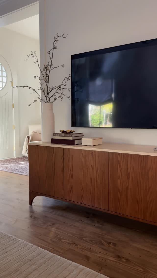 Wooden media console with a white vase and books under a wall-mounted television.