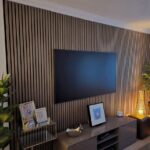 Flat-screen television mounted on a vertical walnut wood slat wall panel with media console.